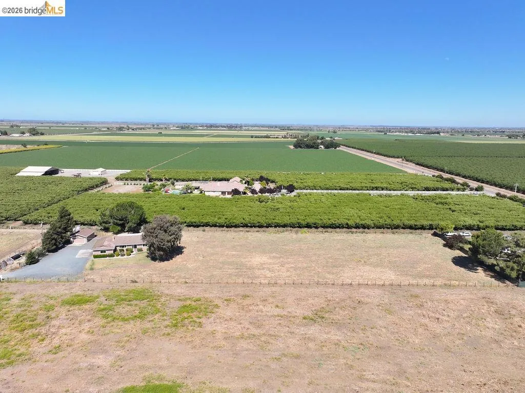 Expansive agricultural property featuring a single-story residence, numerous mature trees, and cultivated fields