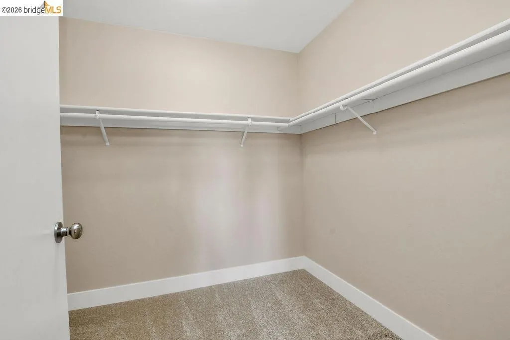 Walk-in closet featuring light beige wall paint, white trim, and a full wrap-around shelving and hanging rod system