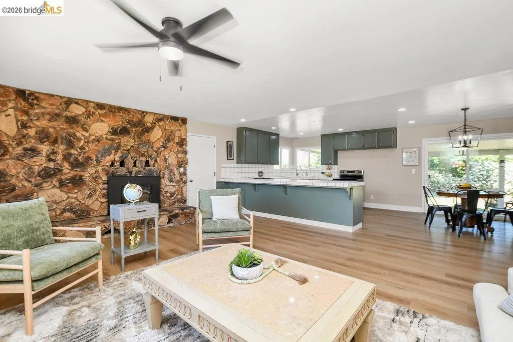 Spacious living area featuring a stone fireplace, wood-finish flooring, and an overhead ceiling fan with lighting
