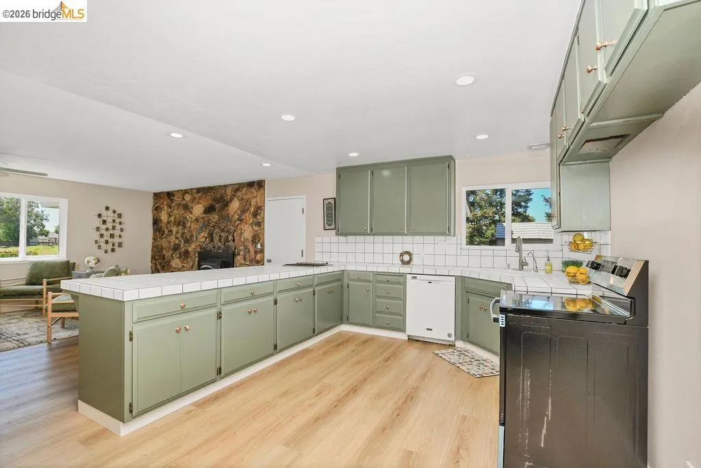 Expansive kitchen featuring sage green cabinetry, white tile countertops, a white tile backsplash, a stainless steel sink, and wood-finish flooring