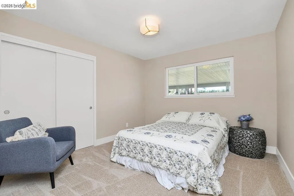 Bedroom featuring light-toned carpeting, a window with exterior views, and a dual-panel sliding closet