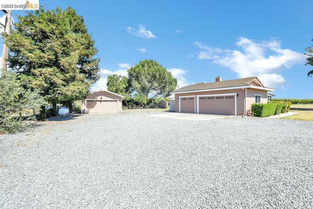 Gravel driveway providing ample parking, featuring a two-car garage and a detached single-car garage