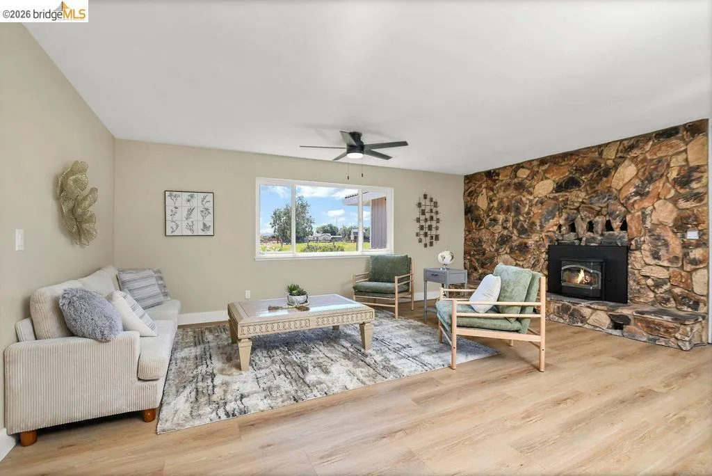 Spacious living area featuring a stone accent wall, fireplace with an insert, wood-finish flooring, and a ceiling fan
