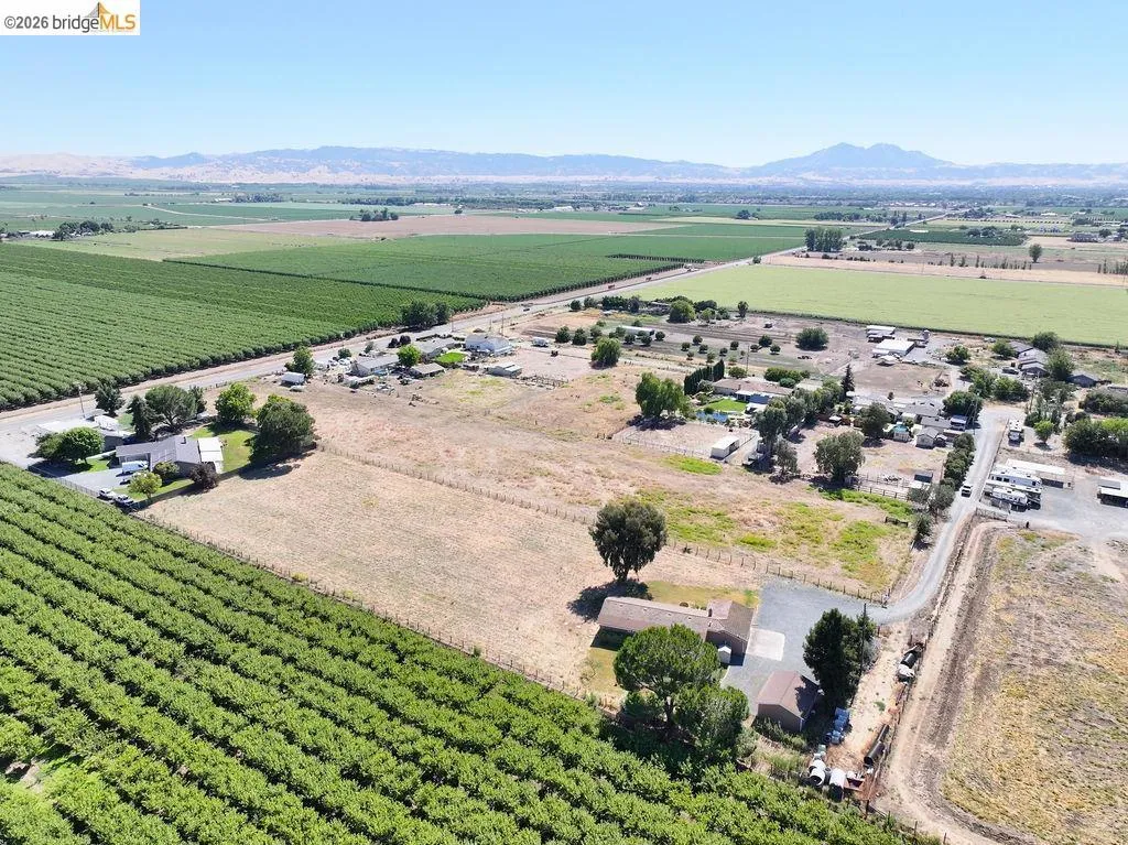 Expansive rural landscape featuring cultivated fields and scattered residential properties, with distant mountains providing a scenic backdrop