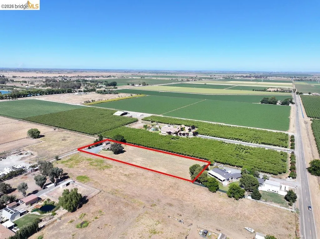 Expansive land parcel featuring a single-story residence, mature trees, and a paved driveway