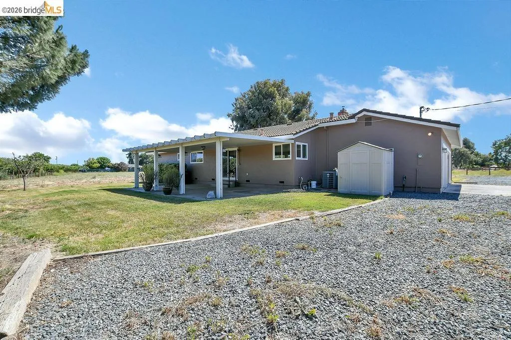 Rear exterior featuring a patio with an attached pergola, stucco siding, and a gravel driveway
