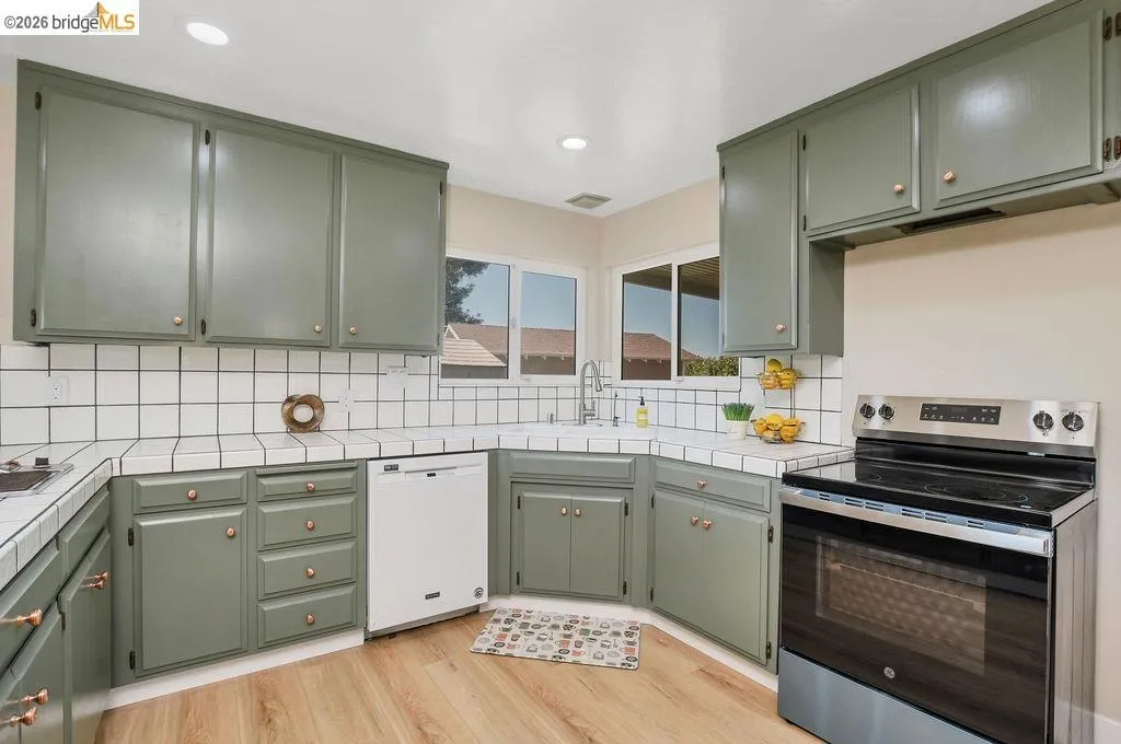 Kitchen featuring wood-finish flooring, recessed lighting, white tile countertops, white tile backsplash, and painted cabinetry with copper-toned hardware