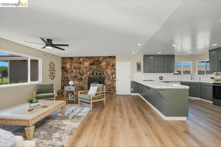 Open-concept living area featuring wood-finish flooring throughout, a stone accent wall with a fireplace, and a contemporary ceiling fan