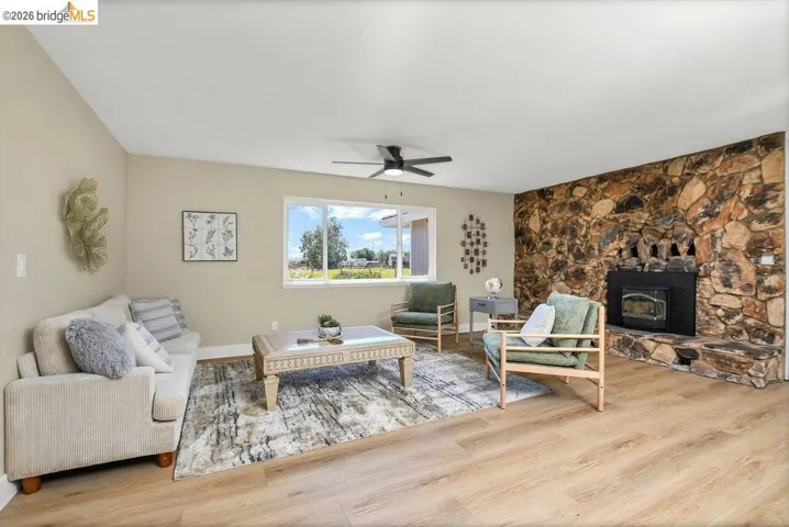 Spacious living area featuring a prominent stone-clad fireplace with a black insert, wood-finish flooring, and a ceiling fan
