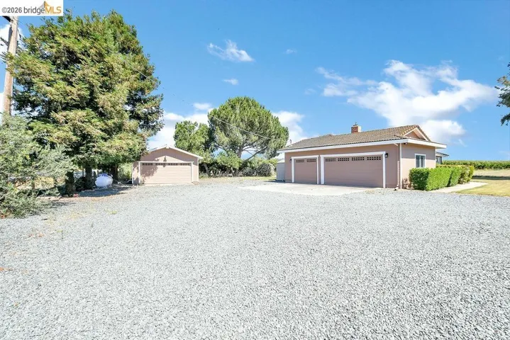 Gravel driveway providing ample parking, featuring a two-car garage and a detached single-car garage