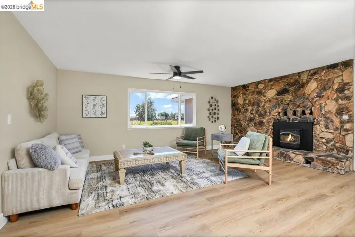 Spacious living area featuring a stone accent wall, fireplace with an insert, wood-finish flooring, and a ceiling fan