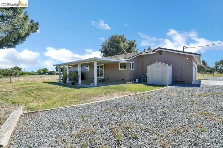 Rear exterior featuring a patio with an attached pergola, stucco siding, and a gravel driveway