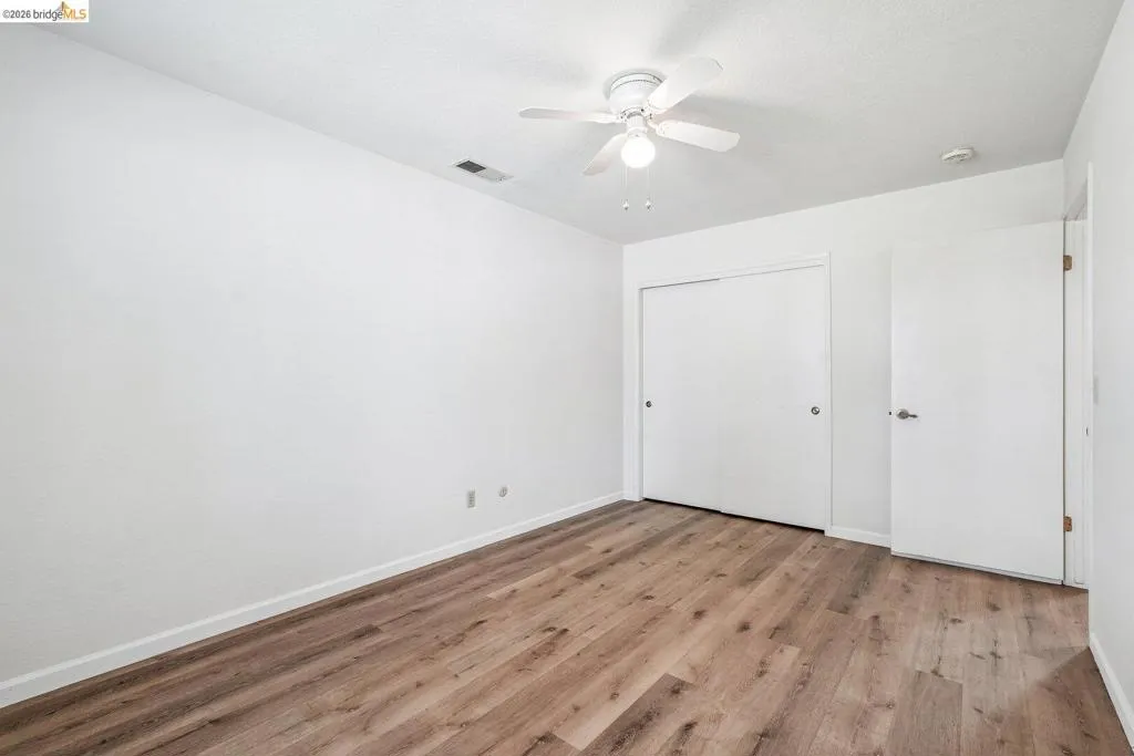 Room featuring wood-finish flooring, white walls, and a ceiling fan with integrated lighting
