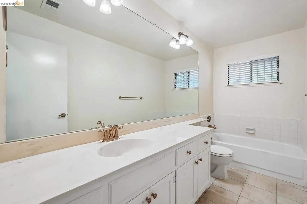 Bathroom featuring a double vanity with white cabinetry, a built-in bathtub with white tile surround, and neutral tile flooring