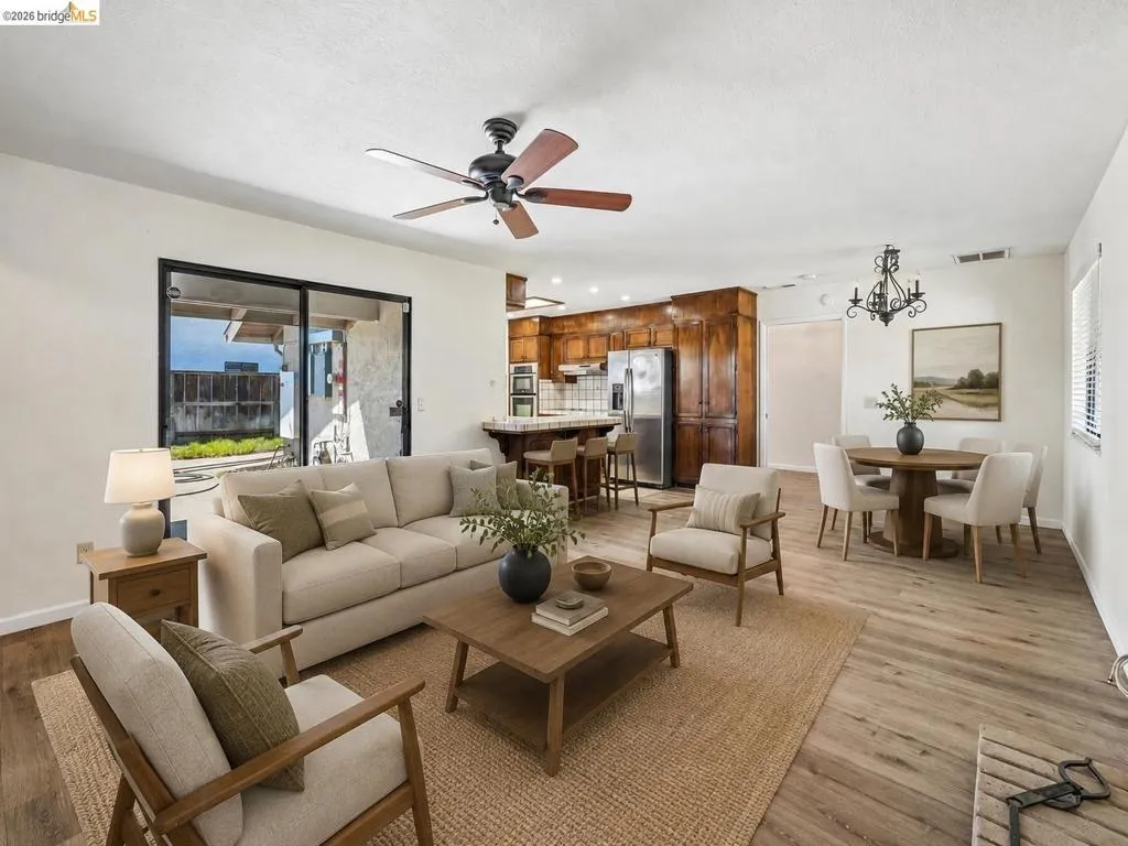 Wood-finish flooring throughout, with a ceiling fan in the living area, and a dining area featuring a chandelier