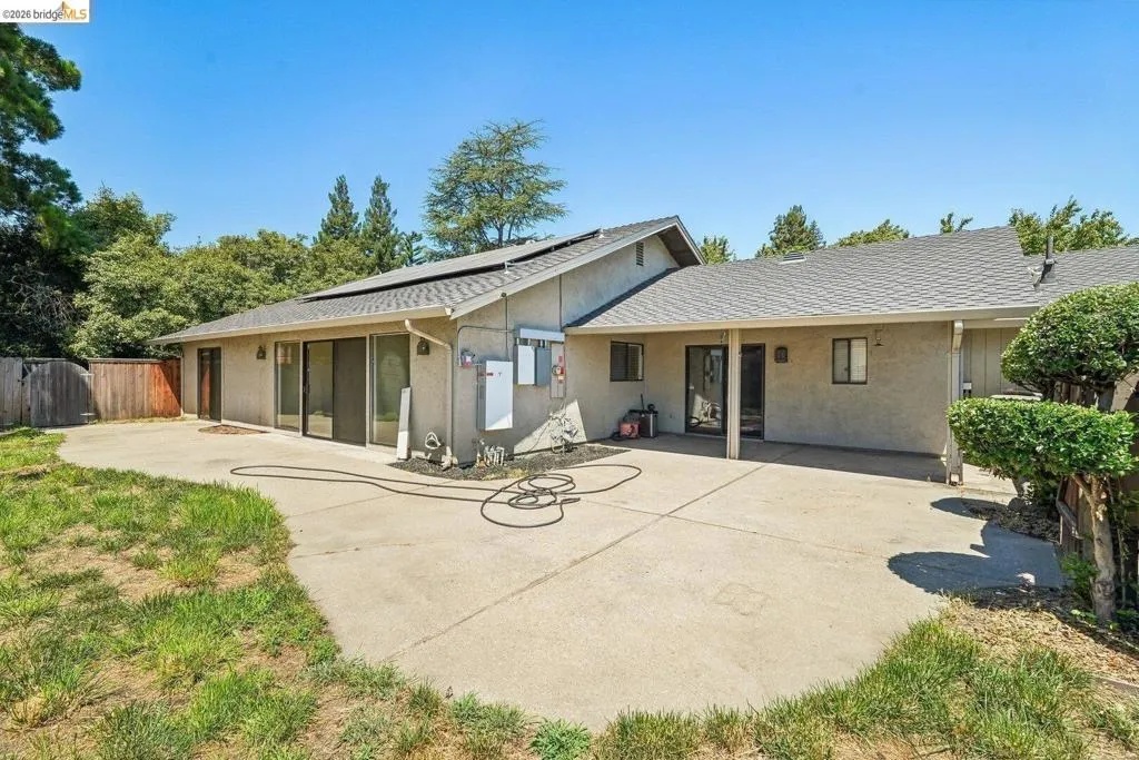 Expansive rear patio area featuring concrete paving, multiple sliding glass doors, and a covered section