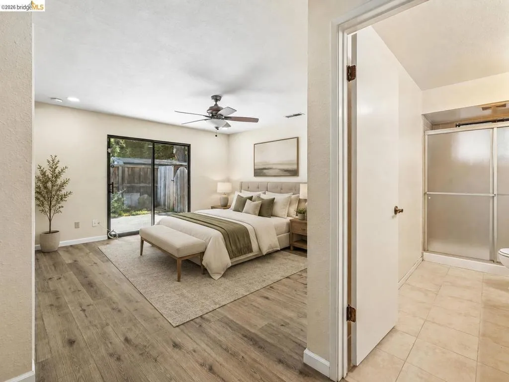 Wood-finish flooring throughout, sliding glass door with exterior access, ceiling fan with integrated lighting, recessed lighting, and an adjacent bathroom with a glass-enclosed shower