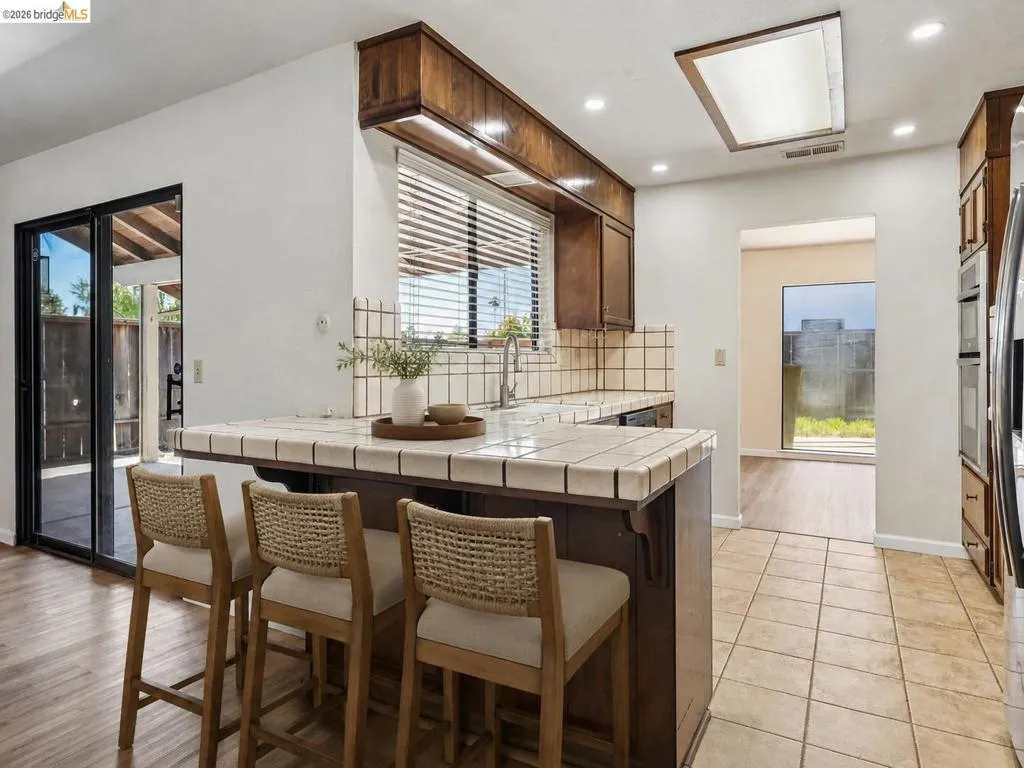Kitchen featuring wood cabinetry, tile countertops, integrated tile backsplash, recessed lighting, and a skylight