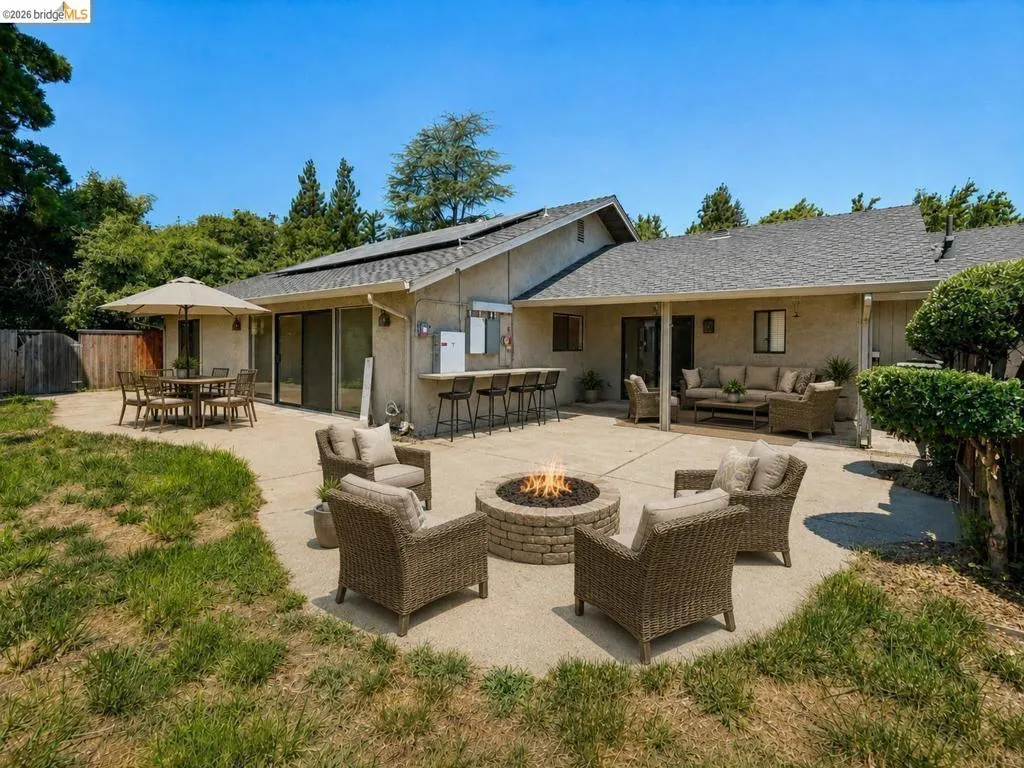 Expansive concrete patio with a built-in fire pit, outdoor bar with seating, and a covered lounge area