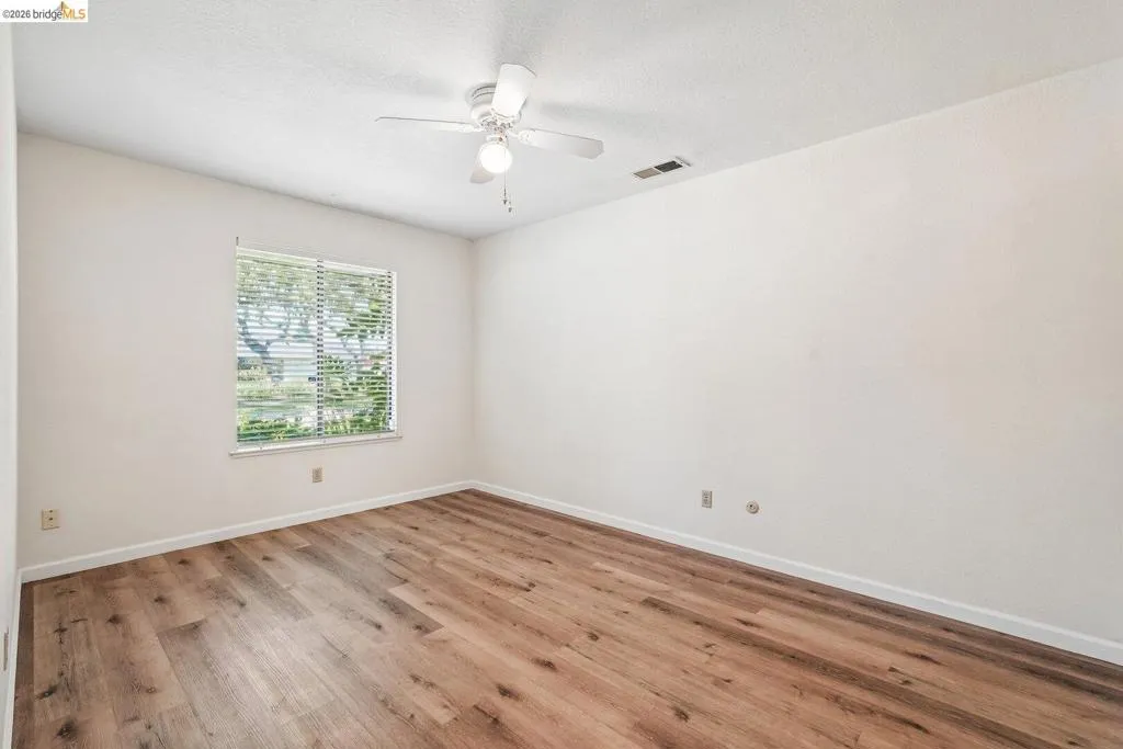 Room with wood-finish flooring, a ceiling fan with light fixture, and a window with horizontal blinds