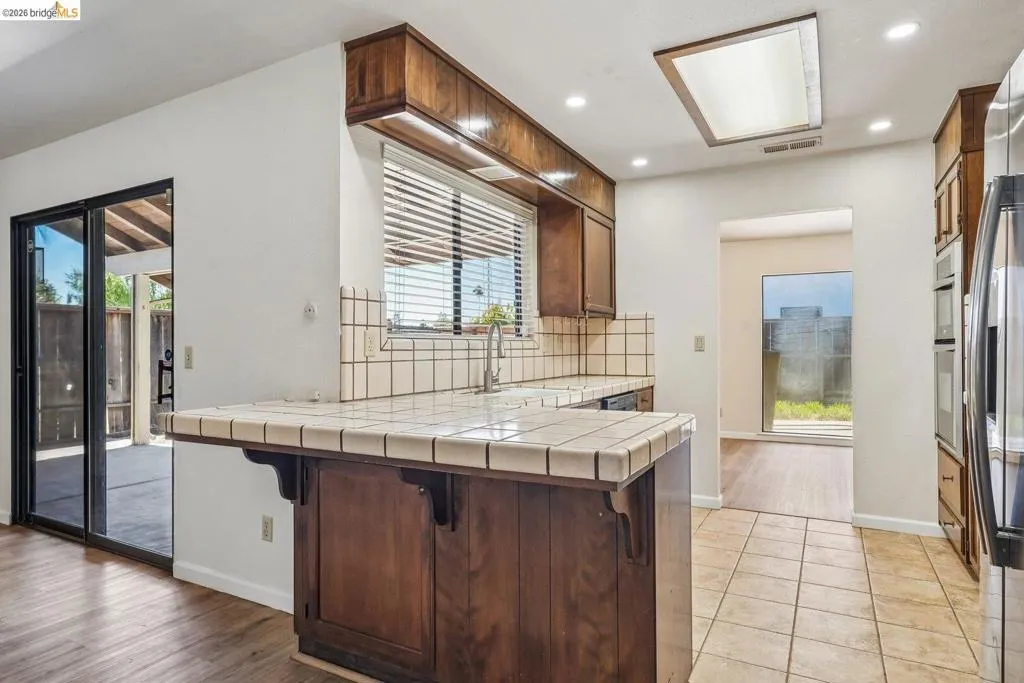 Kitchen featuring a breakfast bar with tile countertop, wood cabinetry, stainless steel appliances, and recessed lighting