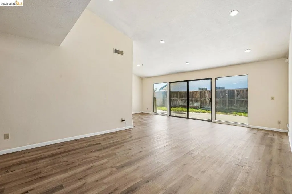 Spacious living area featuring wood-finish flooring, recessed lighting, vaulted ceilings, and a sliding glass door opening to the exterior