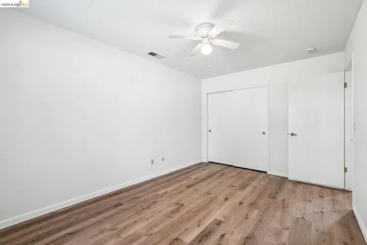 Room featuring wood-finish flooring, white walls, and a ceiling fan with integrated lighting