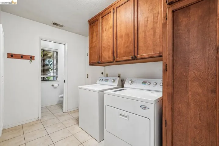 Laundry room featuring wood-finish cabinetry, tile flooring, and integrated appliances