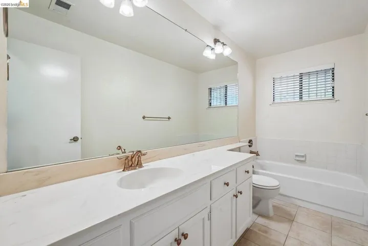 Bathroom featuring a double vanity with white cabinetry, a built-in bathtub with white tile surround, and neutral tile flooring
