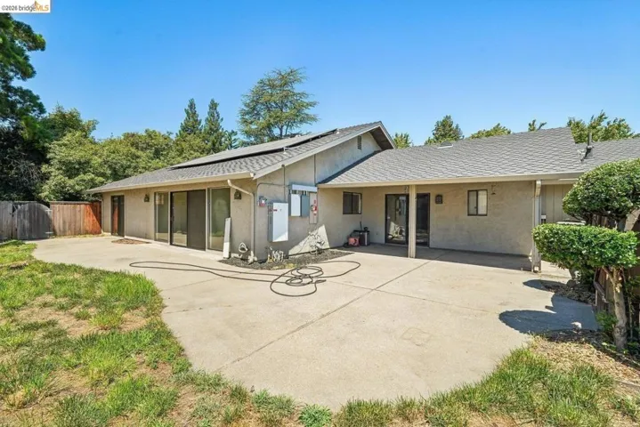 Expansive rear patio area featuring concrete paving, multiple sliding glass doors, and a covered section