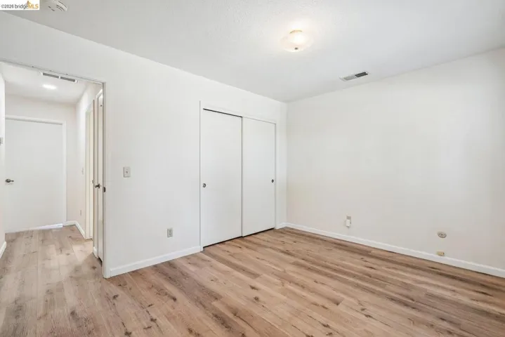 Spacious room featuring wood-finish flooring, white walls, and a ceiling-mounted light fixture
