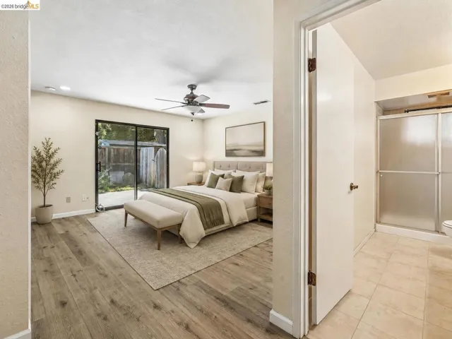 Wood-finish flooring throughout, sliding glass door with exterior access, ceiling fan with integrated lighting, recessed lighting, and an adjacent bathroom with a glass-enclosed shower