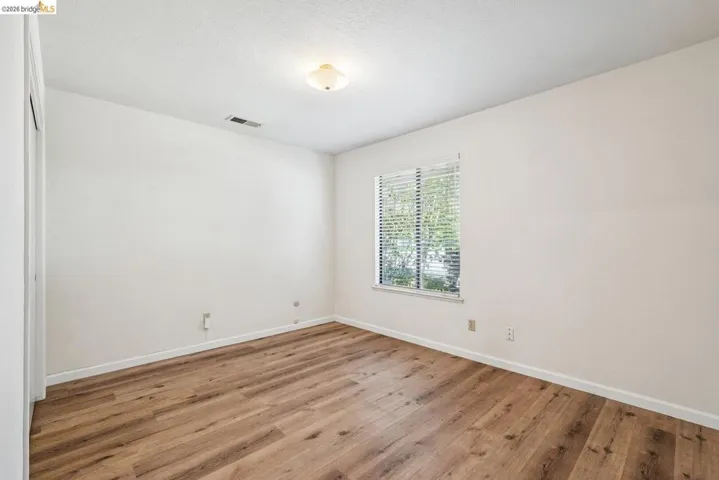 Room with wood-finish flooring, white baseboards, and a window with blinds
