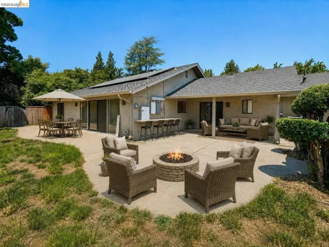 Expansive concrete patio with a built-in fire pit, outdoor bar with seating, and a covered lounge area