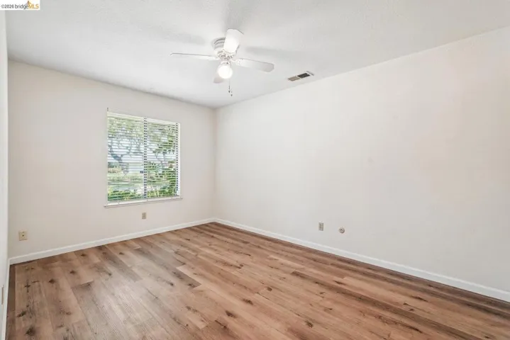 Room with wood-finish flooring, a ceiling fan with light fixture, and a window with horizontal blinds