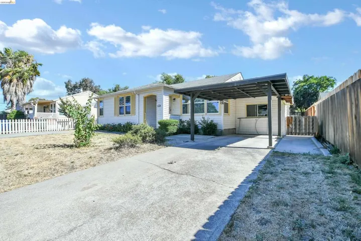 Single-story residence featuring a carport, concrete driveway, and a white picket fence bordering the front lawn