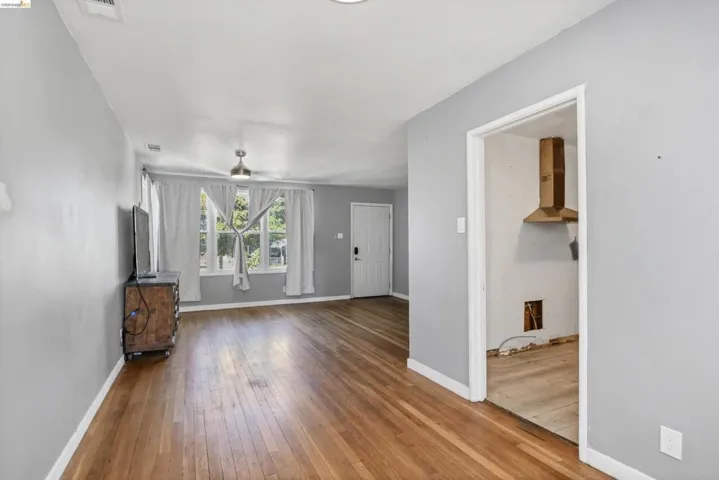 Spacious living area featuring wood-finish flooring, light grey wall paint, a ceiling fan with integrated lighting, and multiple windows
