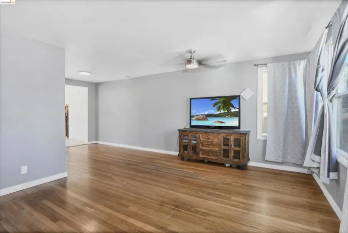 Hardwood flooring throughout featuring light gray walls, a ceiling fan with light fixture, and white trim