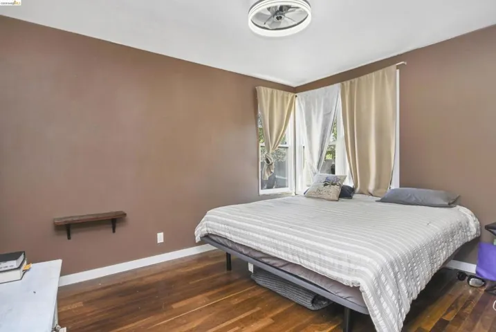 Corner windows with drapery, a ceiling-mounted light fixture, wood-finish flooring, a wall-mounted shelf, and baseboard trim