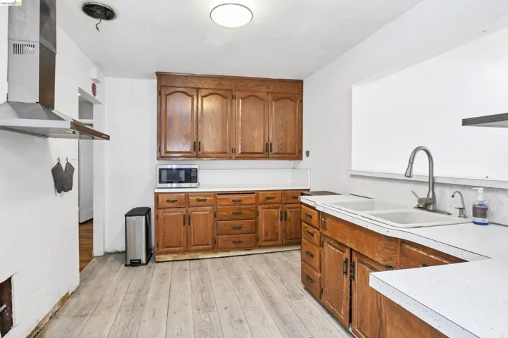 Kitchen featuring wood-finish cabinetry, light-toned wood-finish flooring, white countertops, and a dual basin sink with a gooseneck faucet