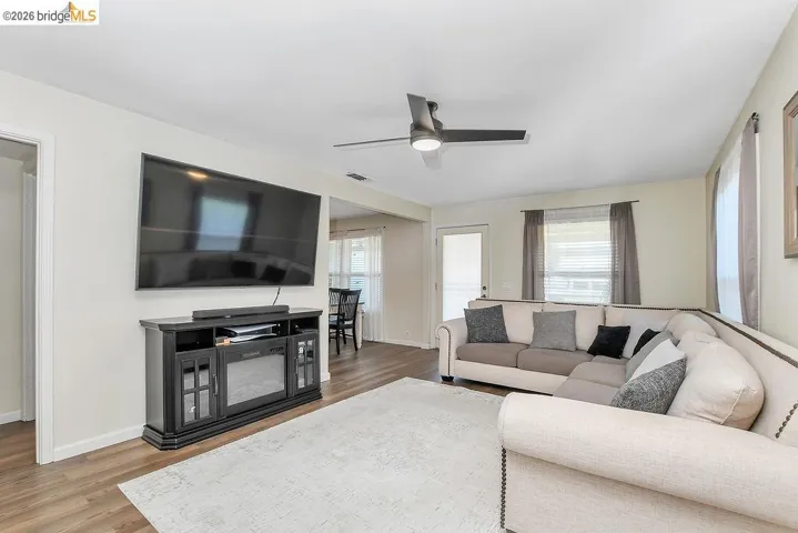Spacious living area featuring vinyl flooring, a contemporary ceiling fan, and abundant natural light from multiple windows.