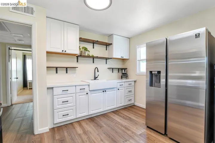Kitchen featuring white cabinetry, a farmhouse sink with a matte black faucet, open shelving, vinyl flooring