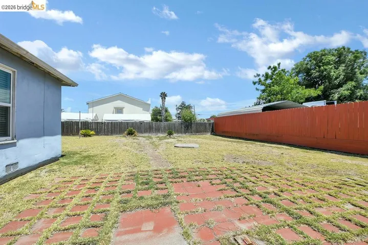 Expansive backyard featuring a red brick paver patio, a partial privacy fence, and a stucco exterior wall