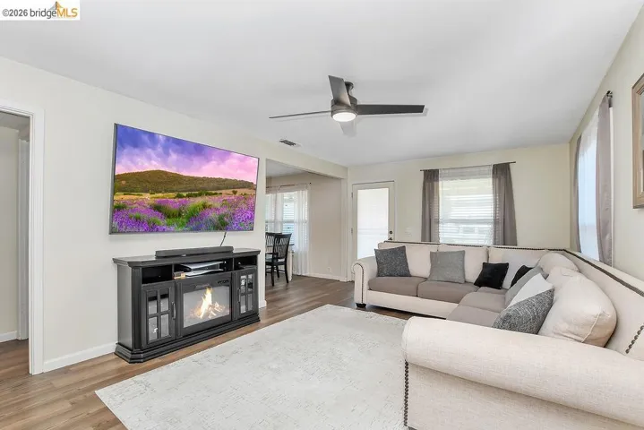 Spacious living area featuring vinyl flooring, a ceiling fan, and ample natural light from multiple windows