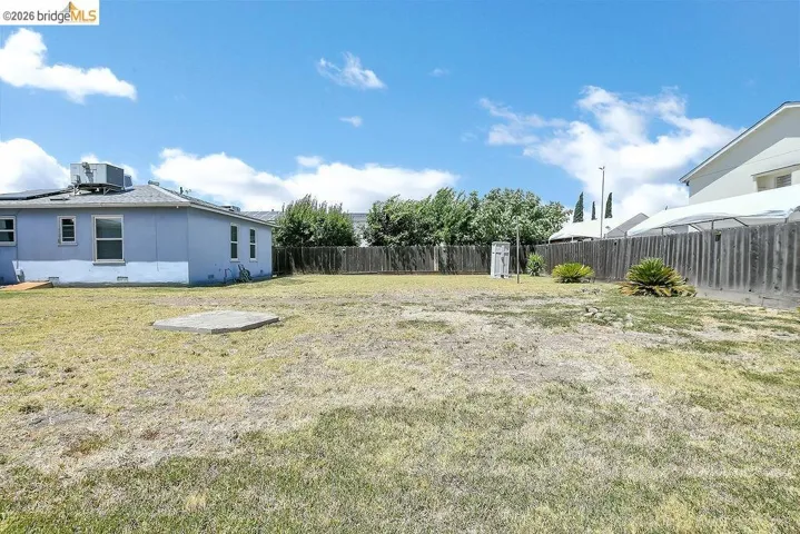 Expansive backyard featuring a concrete pad, partial wood fencing, and established shrubbery