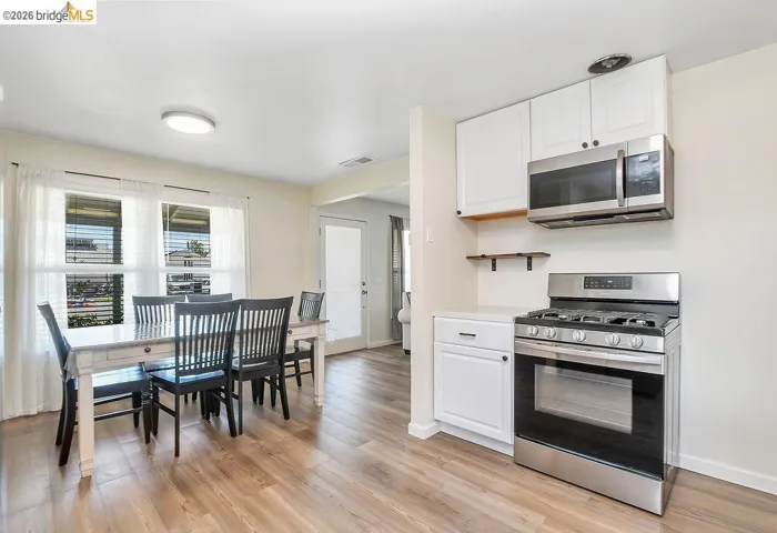 Well-lit kitchen and dining area featuring vinyl flooring, white cabinetry, stainless steel range, and an over-the-range microwave