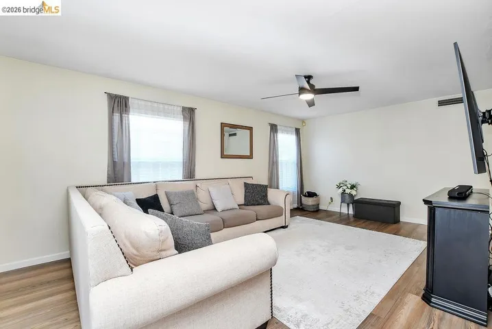Spacious living area featuring vinyl flooring, light-colored walls, a ceiling fan, and multiple windows providing natural light.