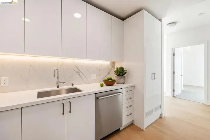 Modern kitchen area featuring a stainless steel undermount sink, sleek white cabinetry, and a marbled backsplash