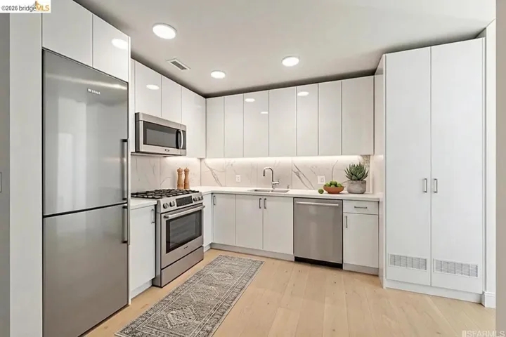 Modern kitchen featuring white flat-panel cabinetry, stainless steel appliances, light wood-finish flooring, recessed lighting, and an integrated marble-patterned backsplash