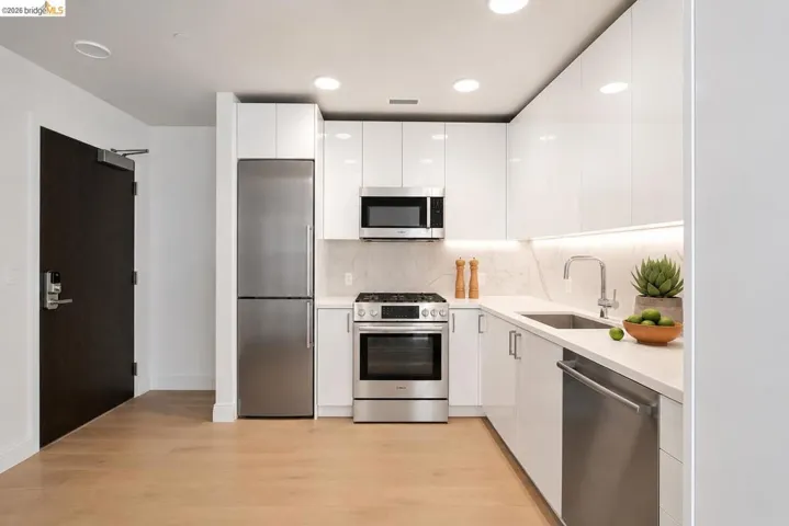 Modern kitchen featuring stainless steel appliances, white flat-panel cabinetry, light-toned wood-finish flooring, and recessed lighting